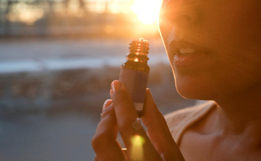 "A woman enjoys the scent of an essential oil from a small amber bottle at sunset, highlighting the calming and therapeutic benefits of aromatherapy.